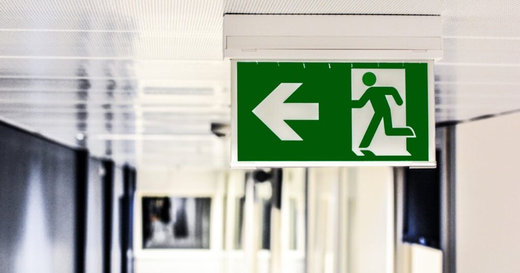 pexels-photo-134065 Green emergency exit sign with directional arrow in a hallway.