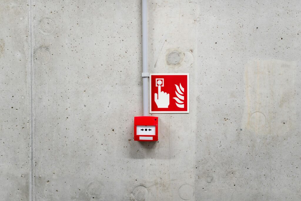 pexels-photo-20614571-20614571 Red emergency fire alarm on a gray concrete wall in Poznań, enhancing safety awareness.