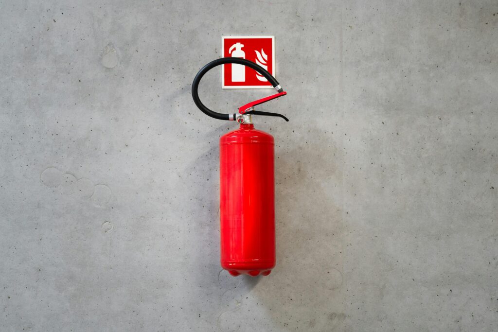 pexels-photo-21299748-21299748 A red fire extinguisher mounted on a concrete wall indoors with emergency signage.
