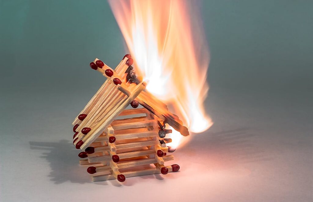 pexels-photo-358511 Close-up of a small matchstick house ablaze, showcasing flame and heat.